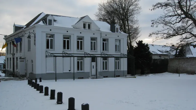 Bâtiment blanc à deux étages et lucarnes, avec une marquise en fer forgé, sur une place enneigée bordée de potelets noirs