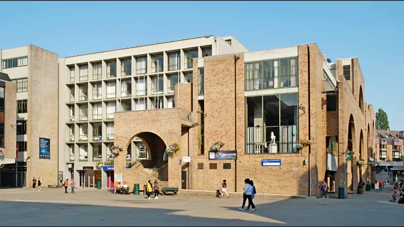 Façade en briques des Halles universitaires, place de l'Université à Louvain-la-Neuve, avec son arche et ses grandes baies vitrées, sous un ciel bleu