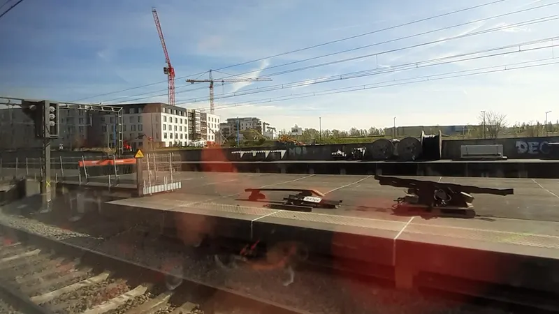 Quai de la future halte de Braine-Alliance vu depuis un train, avec des immeubles et des grues à l'arrière-plan, pendant le chantier en avril 2022
