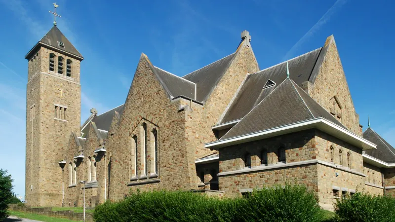 L'église Saint-Géry de Limelette, bâtiment en pierre avec un clocher carré et de hautes toitures en ardoise, sous un ciel bleu