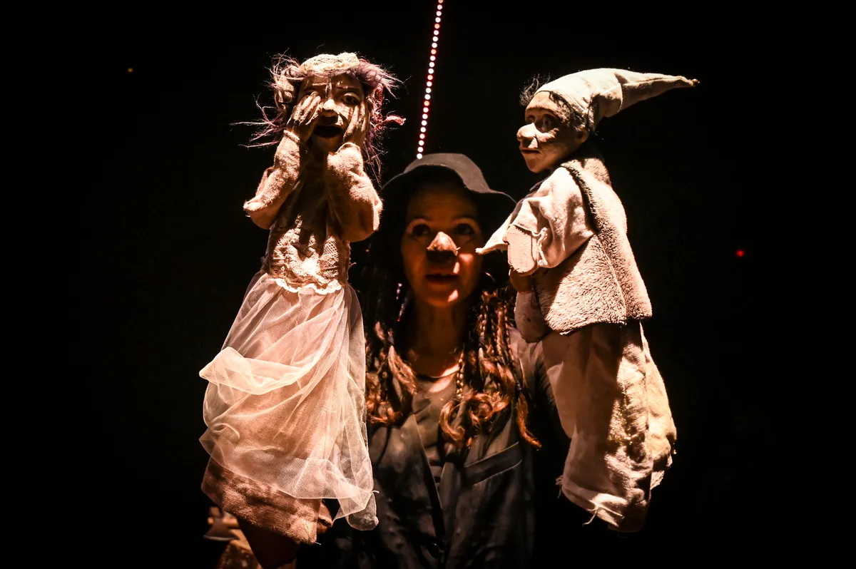 Comédienne tenant deux marionnettes de chiffon aux visages expressifs, sur fond noir