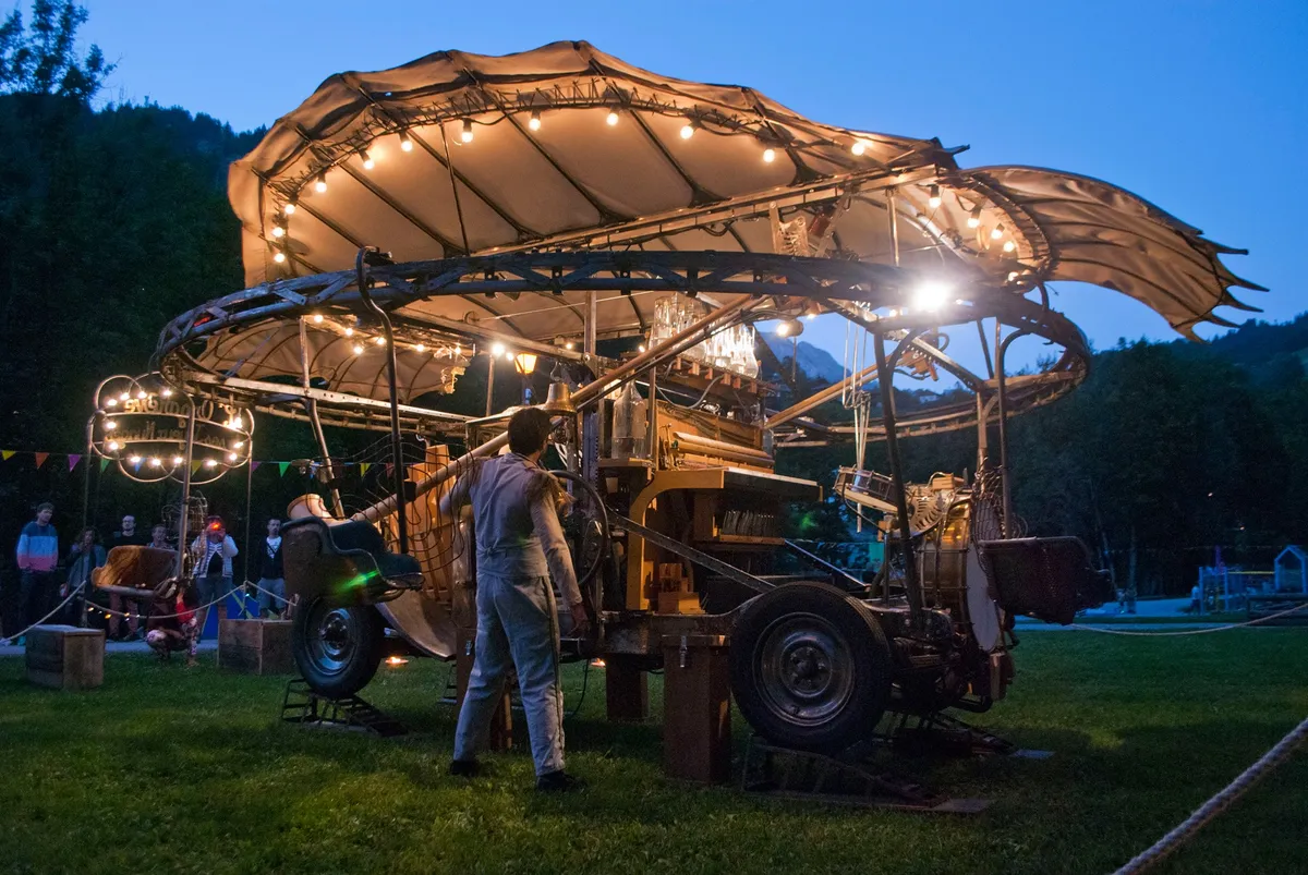 Manège circulaire illuminé en forme de nuages autour d'une voiture-orchestre, de nuit, dans un parc