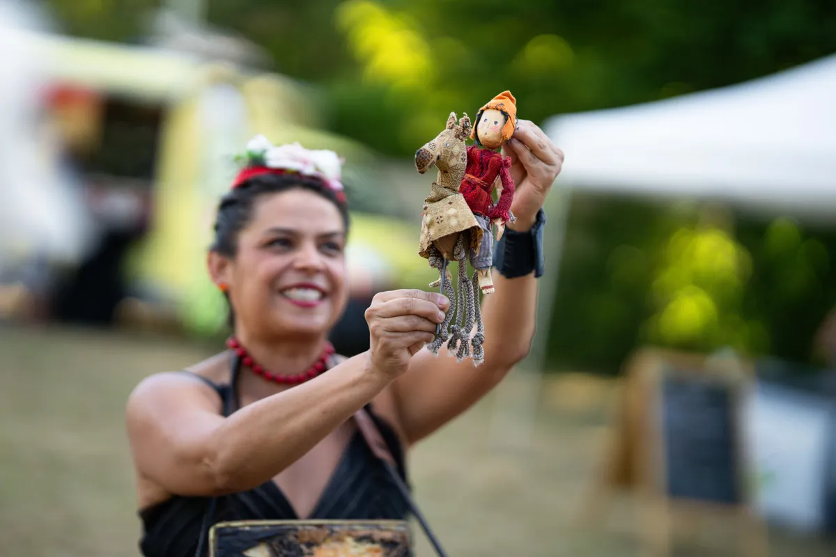 Petit théâtre miniature ouvert dans une valise, tenu par une artiste souriante, en plein air