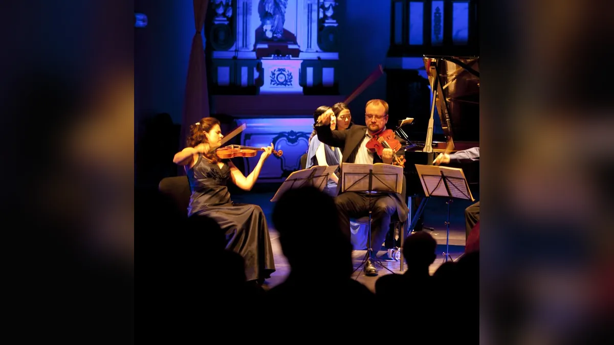 Quatuor à cordes et piano en concert sur une scène éclairée en bleu, public en silhouette au premier plan