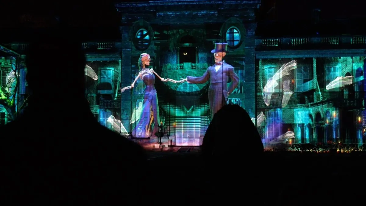 Projection géante sur la façade du château d'Hélécine : deux personnages en tenue de mariage se donnent la main devant des spectateurs en silhouette