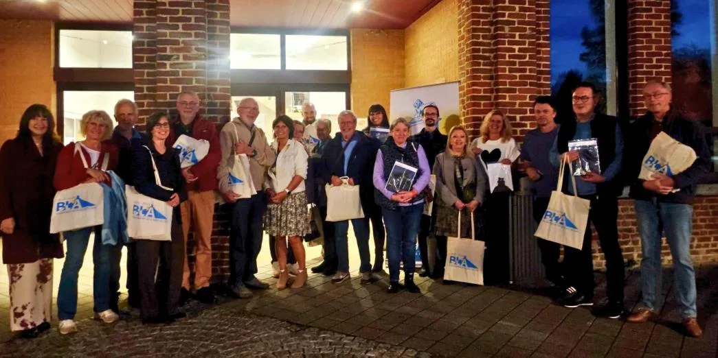 Une vingtaine de personnes posent le soir devant la façade en briques de l'École des Arts, la plupart avec un sac en toile aux couleurs de l'anniversaire de la Butte